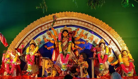 Durga Puja pandal idol under a golden carved arch, green backdrop