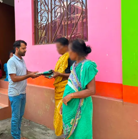 Volunteer distributing clothes to two women during Durga Puja
